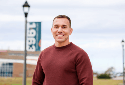 White male student standing on campus near a flag pole