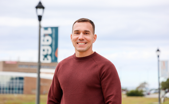 White male student standing on campus near a flag pole