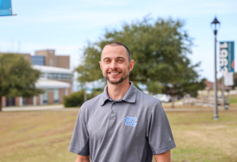 a male standing outside on campus wearing a grey shirt with the UNC logo