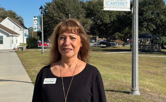 a lady standing outside on campus with a flagpole behind her.