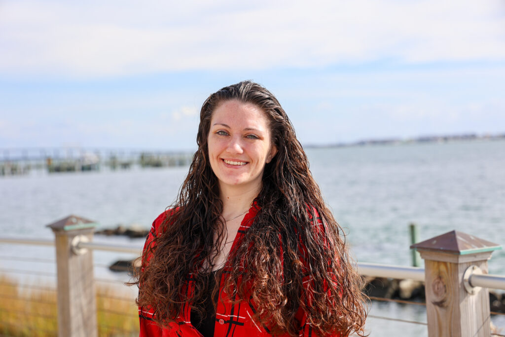 a female student standing outside by the water in a red shirt