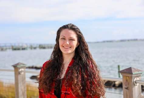 a female student standing outside by the water in a red shirt
