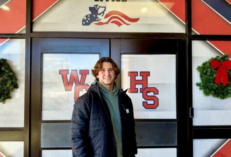 A male student standing outside of West Carteret high school doors with the logo showing