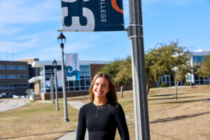 A female student on campus outside with the building and flag poles in the background