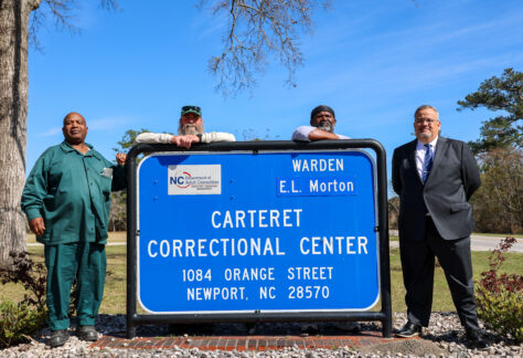 Four men stand behind a Carteret Correctional Center sign in Newport, North Carolina, representing a partnership between the correctional facility and Carteret Community College.