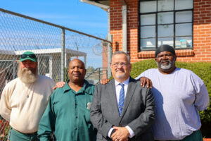 Four men, including a warden and program participants, stand together outside Carteret Correctional Center, highlighting a collaborative reentry and education initiative.