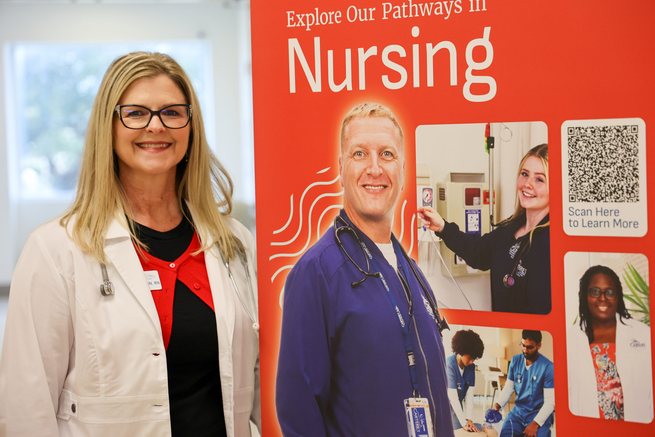 A woman in a lab coat stands next to a bright orange display promoting nursing pathways, featuring images of healthcare workers and a QR code for more information.