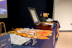 Phi Theta Kappa honor cords, medals, and certificates displayed on a table alongside awards and ceremony materials.