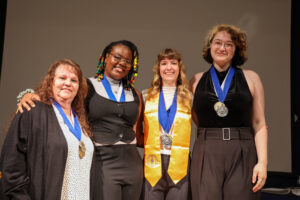 BV4A0500 Four Phi Theta Kappa members stand together smiling, wearing medals and honor stoles during the induction ceremony.