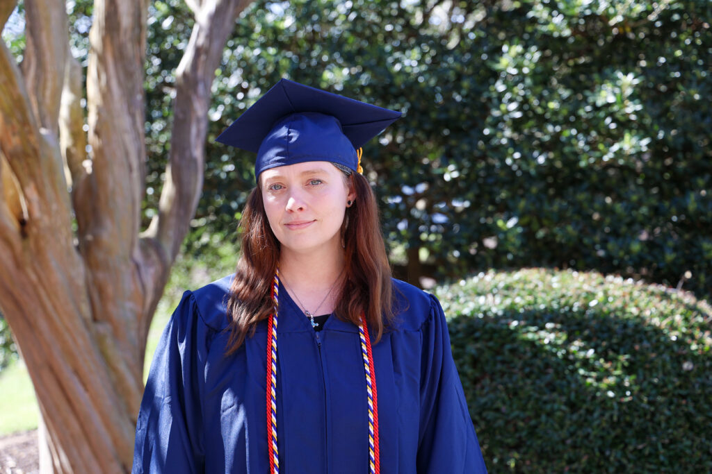 Female student in a blue cap and gown standing outside.