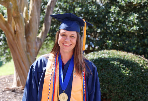 A female student in a graduation blue cap and gown outside