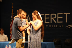A female student standing on stage with her husband and daughter getting pinned